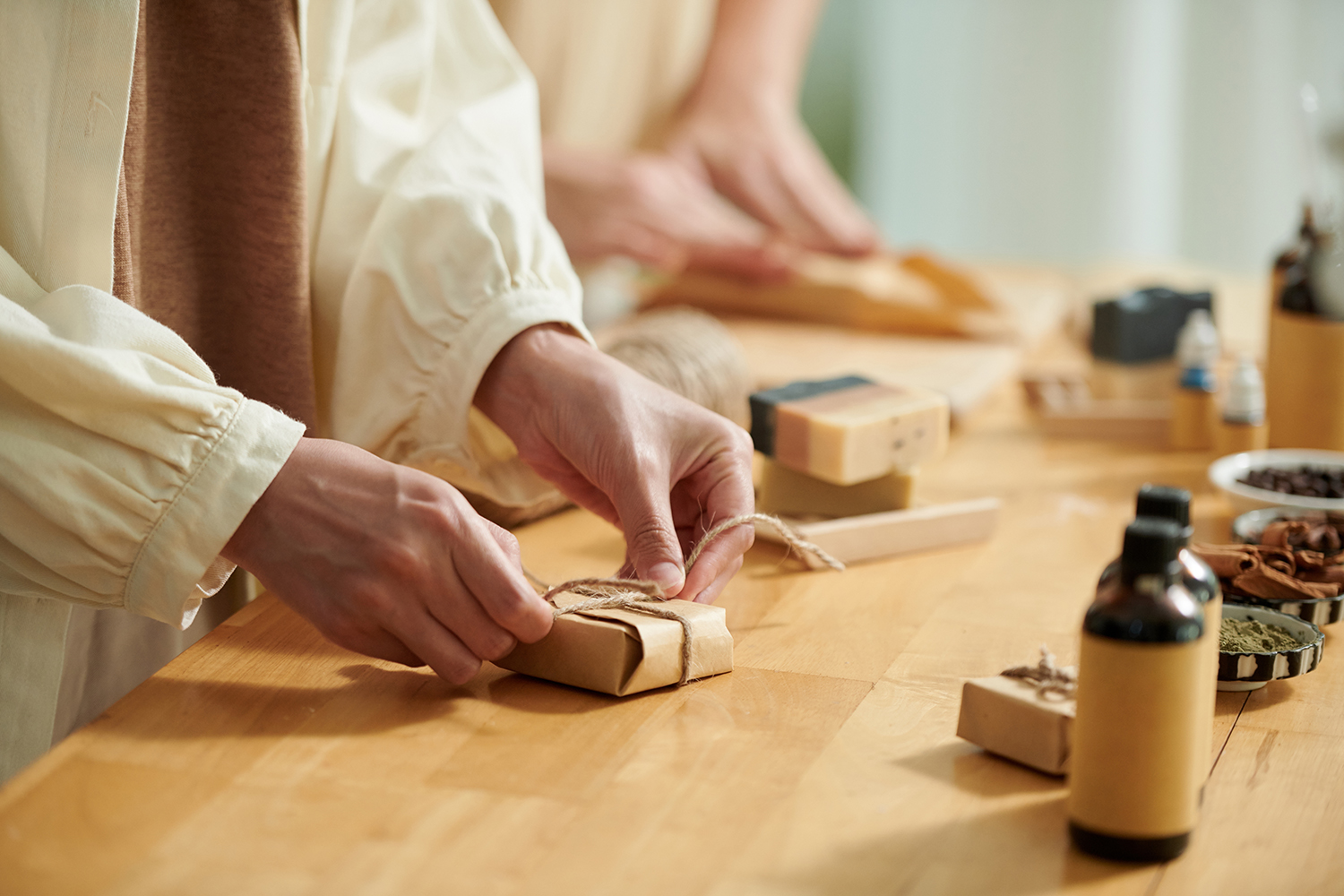 Hands of women wrapping handmade soap bars in craft paper